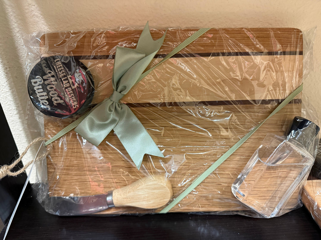 Handmade wooden charcuterie board gift set wrapped with a green ribbon, with wood butter, a cheese knife and a spreader